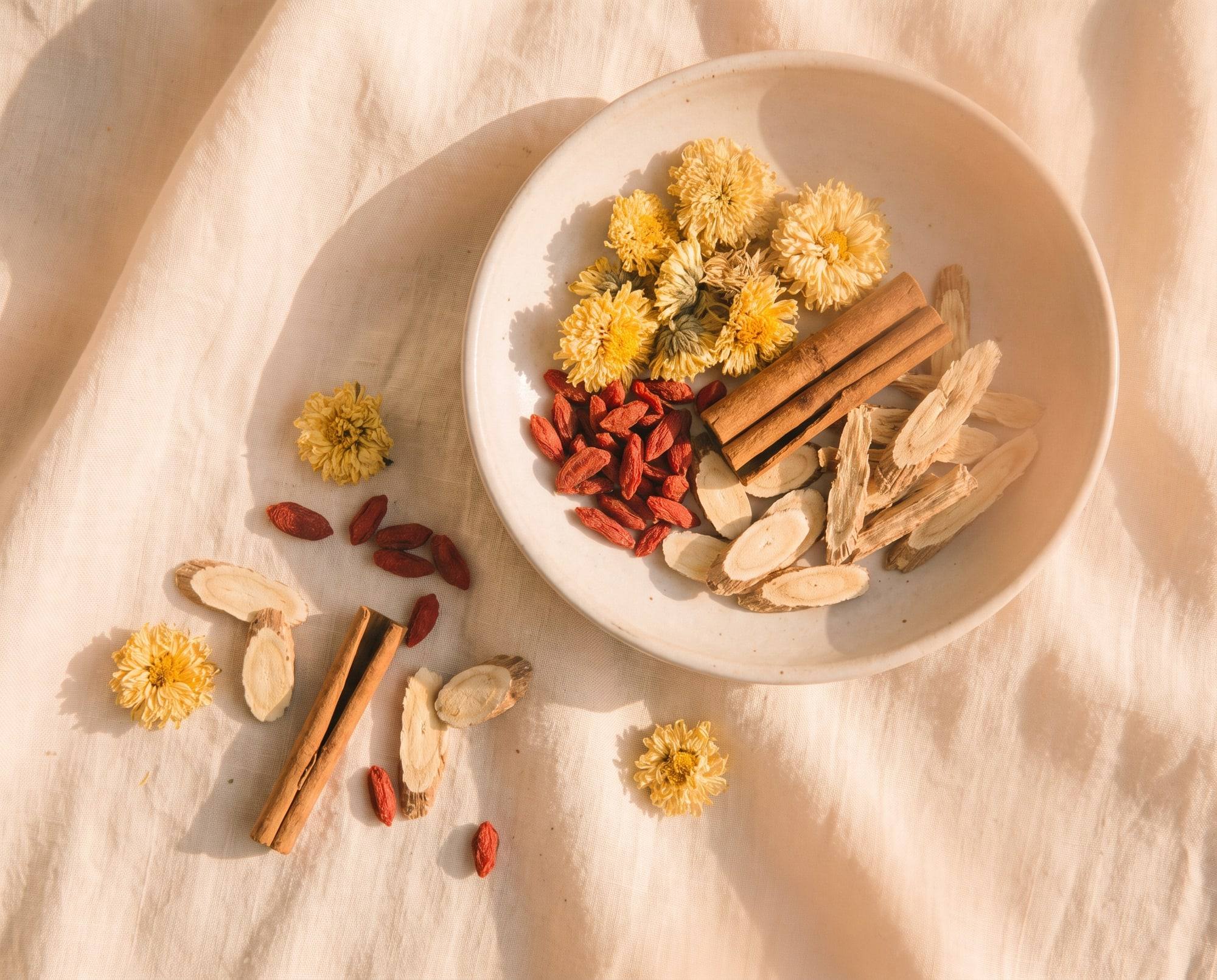 Dried Chinese herbs in a ceramic dish on linen: chrysanthemum, goji berries, cinnamon bark and astragalus