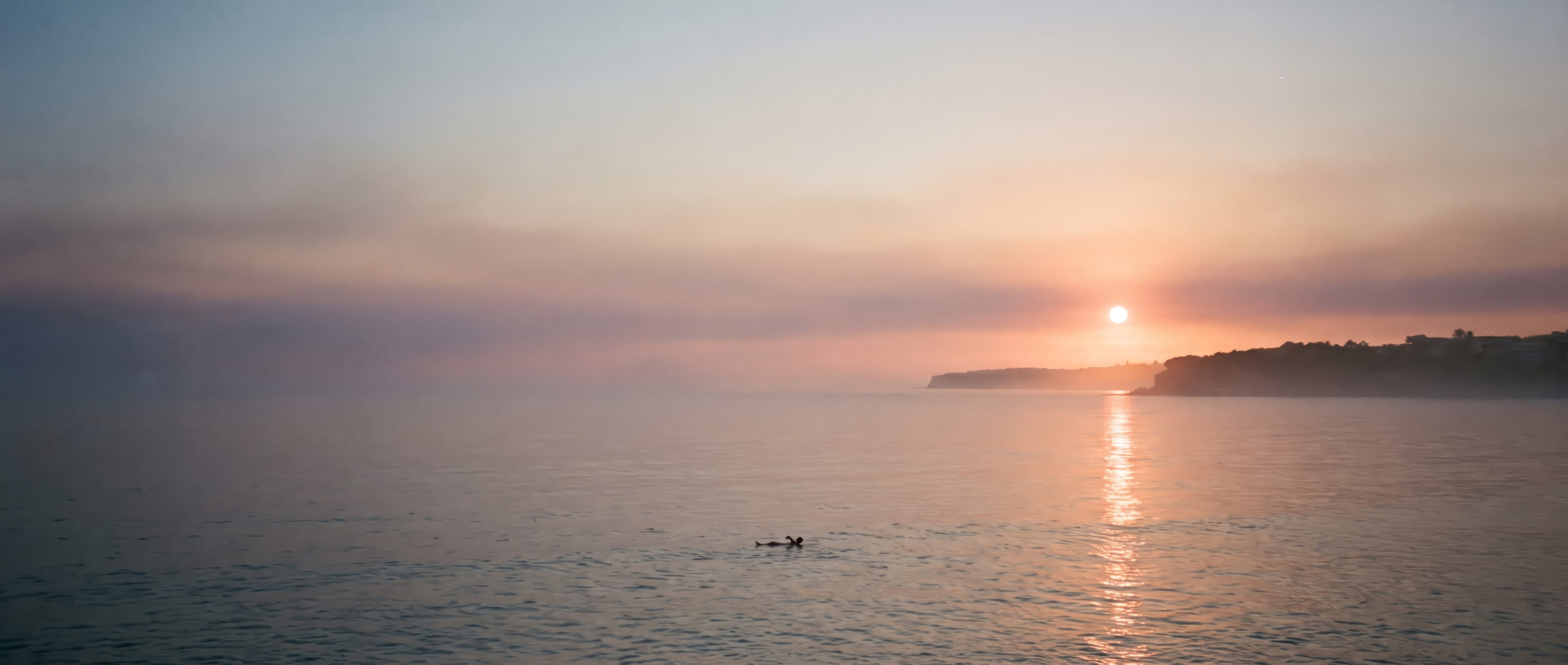 A swimmer floating on their back in calm water off Bondi at dawn, the low sun lighting a path across the sea